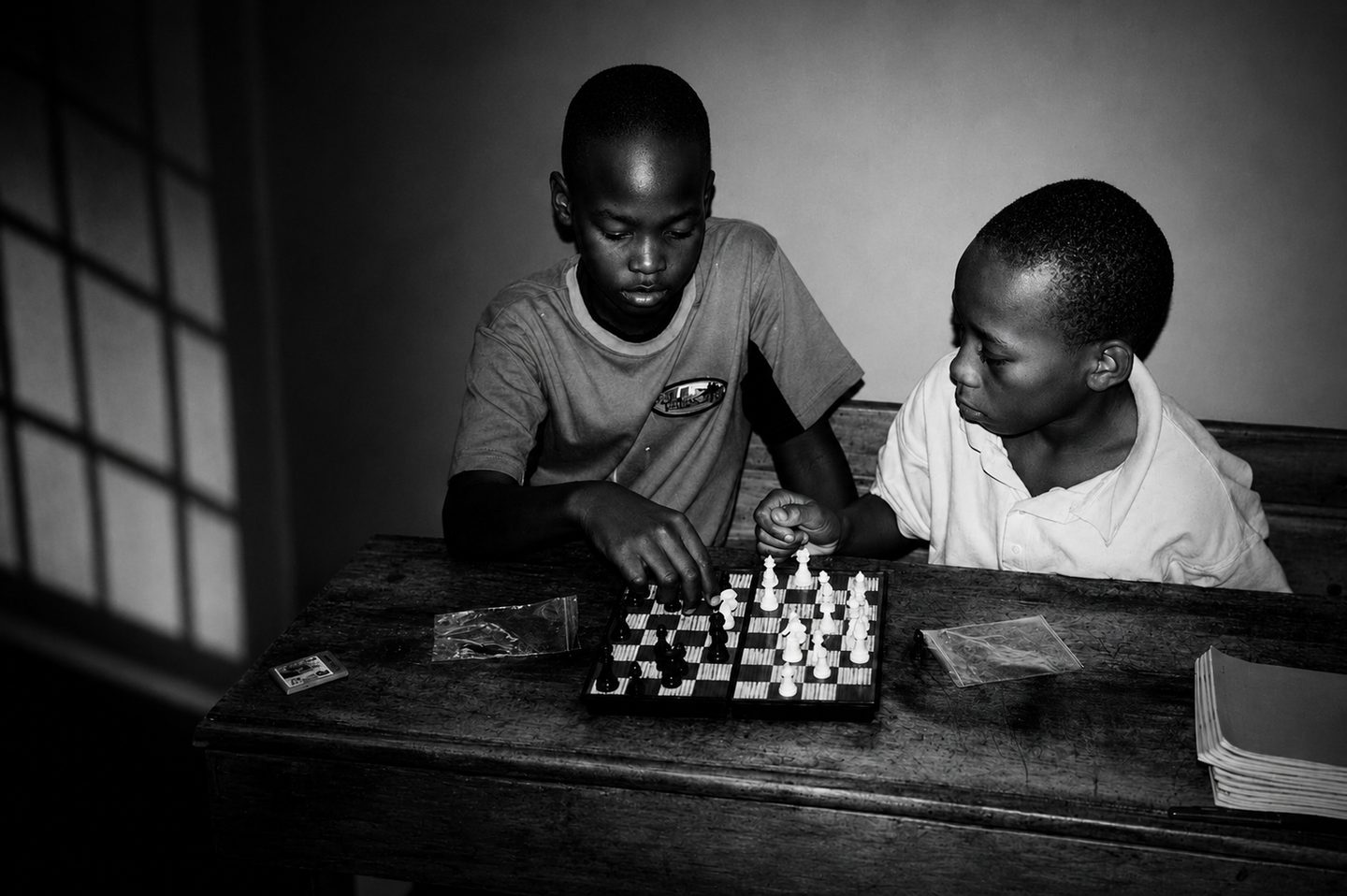 Two boys focused over a game of chess, one studying the other's move.